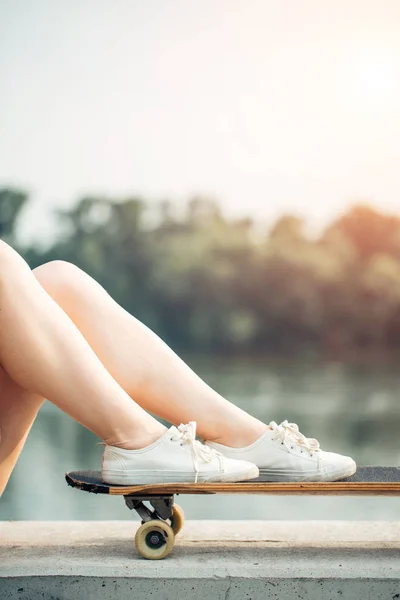 Close-up van trendy vrouwelijke benen ontspannen op een longboard. Ripped jeans mode — Stockfoto