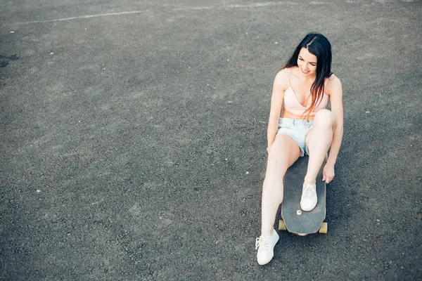 Mooi jong meisje met tatoeages zit op longboard bij zonnig weer — Stockfoto