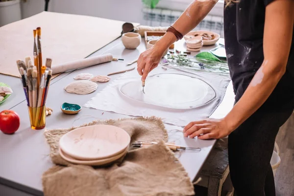 Maestro ceramista frota un plato de arcilla al horno. Un taller creativo . — Foto de Stock