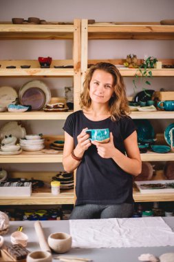 Kadın tezgahı bitmiş çatal bıçaklarla, gülümseyen seramikçi işyeri fırınlanmış fincanlarla