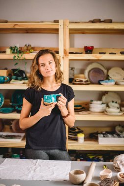 Kadın tezgahı bitmiş çatal bıçaklarla, gülümseyen seramikçi işyeri fırınlanmış fincanlarla