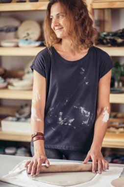 Sanatçı, atölye ile kaplı büyük gri oklavayı kullanarak çiğ çamur yuvarlıyor.