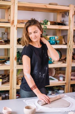 Sanatçı, atölye ile kaplı büyük gri oklavayı kullanarak çiğ çamur yuvarlıyor.