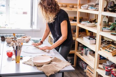 Kadın çömlekçi ustası seramik ürünlerle birlikte masayı topluyor.