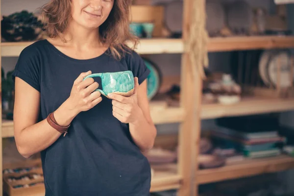 Frauenstand mit fertigen Utensilien, lächelnder Keramiker-Arbeitsplatz mit gebackenen Tassen — Stockfoto