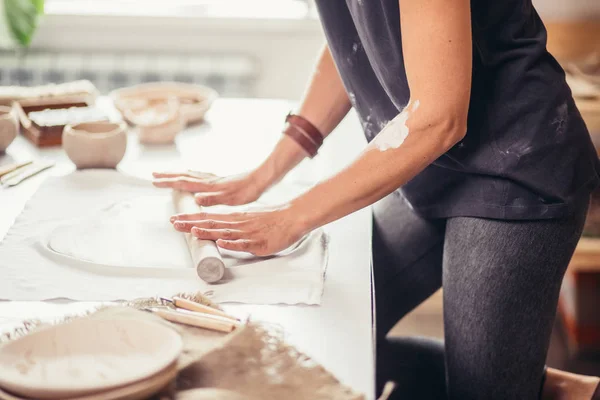 Художник катает сырую глину, используя большую серую скалку на столе, покрытом в мастерской — стоковое фото