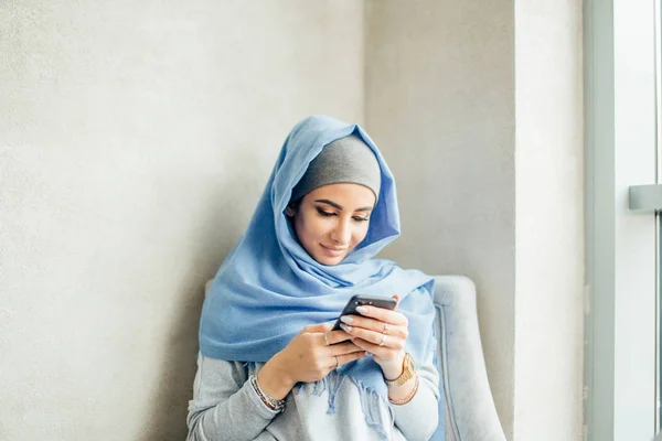 Mujer joven sentada y sosteniendo teléfono móvil — Foto de Stock