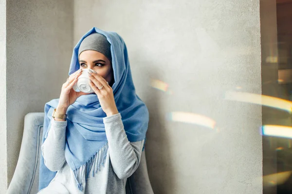 Красивая молодая мусульманка с чашкой кофе или чая в действии — стоковое фото