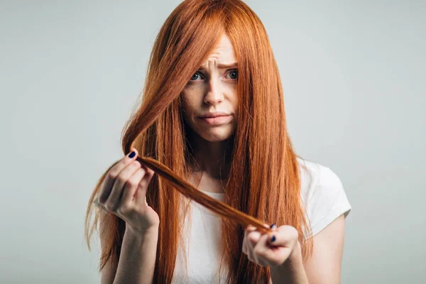 Triste ragazza rossa che tiene i capelli danneggiati guardando la fotocamera. — Foto Stock