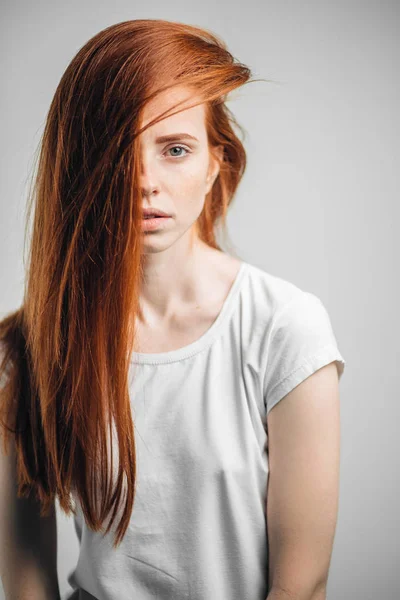 Jovem menina ruiva bonita com sardas olhando para a câmera sorrindo tocando o cabelo — Fotografia de Stock