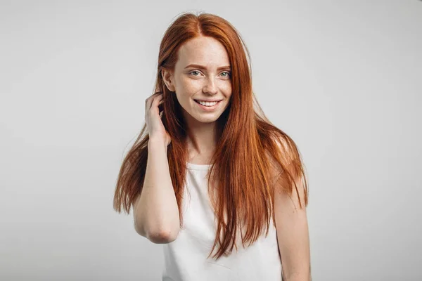 Девушка улыбается с закрытыми глазами касаясь ее рыжие волосы на белом фоне — стоковое фото