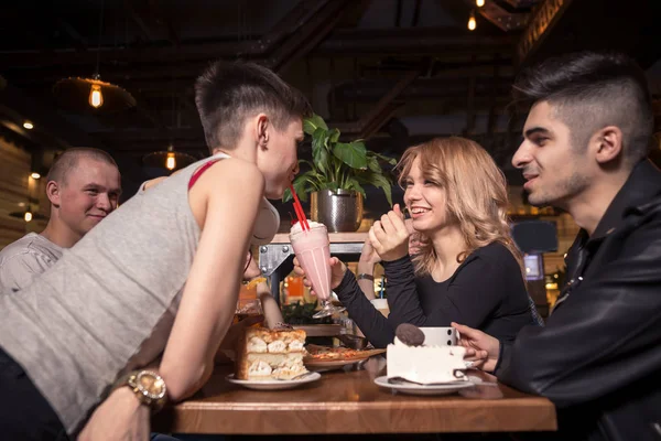 Молодая женщина пьет молочный коктейль, сидя с друзьями в кафе — стоковое фото