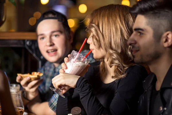 Mujer joven bebiendo batido mientras está sentada con amigos en la cafetería — Foto de Stock