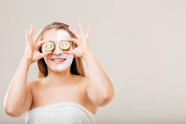 Vacker blond flicka i handduk tar kiwi innan ögonen på vit — Stockfoto