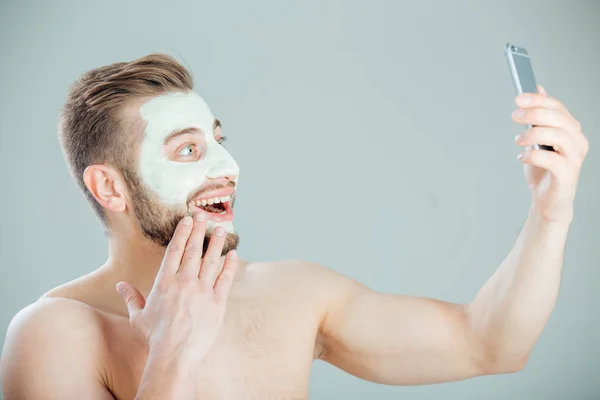 Joven y hermoso hombre con Mascara Purificante en su cara haciendo selfie —  Fotos de Stock
