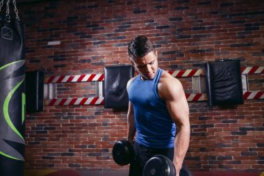 kaslı vücut geliştirmeci biri dumbbells ile yapıyor