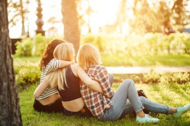 Çim ve hugs üzerinde oturan üç güzel kadın arkadan görünüm