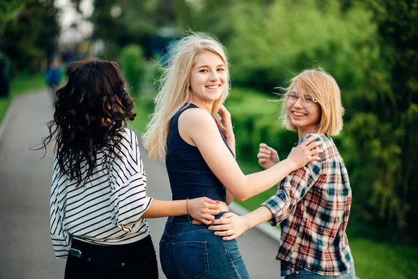 Three girls having fun in the sunset park. rear view — Stock Photo, Image