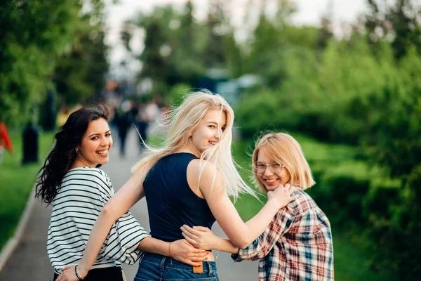 Back view of three beautiful women sitting on grass and hugs — Stock Photo, Image