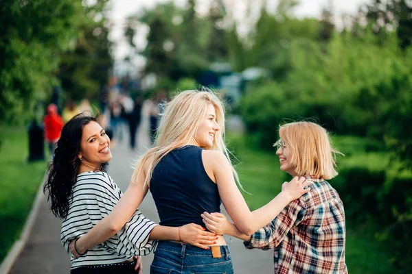 Three girls having fun in the sunset park. rear view — Stock Photo, Image