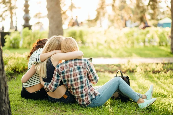 Baksidan på tre vackra kvinnor sitter på gräset och kramar — Stockfoto