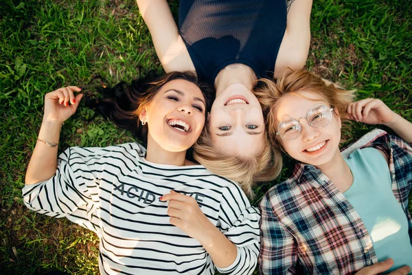 Vue de dessus des amis élégants regardant la caméra et souriant tout en étant couché sur l'herbe — Photo