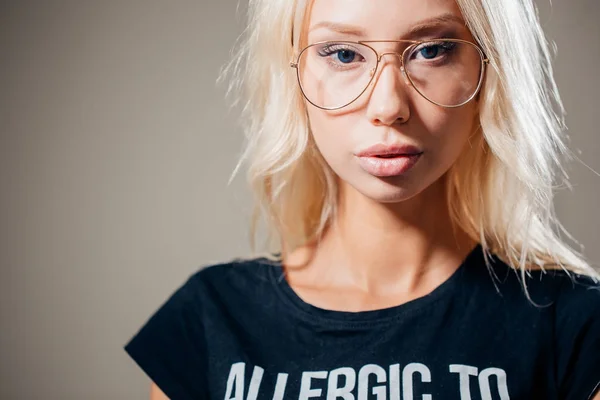 Gelukkig casual jonge vrouw in glazen op zoek op grijze achtergrond — Stockfoto