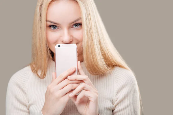 Женщина закрывает рот чистым экраном смартфона на сером фоне — стоковое фото