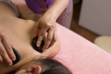 Masaj terapisti masaj masasına uzanmış bir kızın sırtına spa taşı koyuyor.