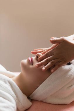 Kapalı gözlü bir kadın kaplıcada yüz veya kafa masajı yaptırıyor.