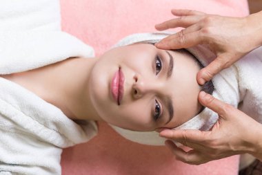 Kapalı gözlü bir kadın kaplıcada yüz veya kafa masajı yaptırıyor.