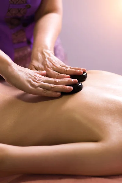 Massaggiatore mettendo pietre spa sul retro della ragazza sdraiata sul tavolo da massaggio — Foto Stock