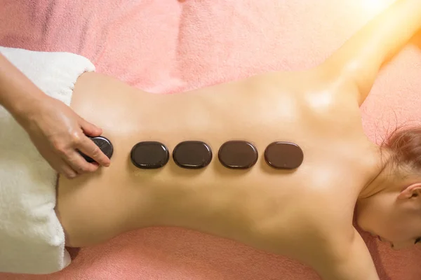 Массажист кладет спа-камни на спину девушки лежащей на массажном столе — стоковое фото