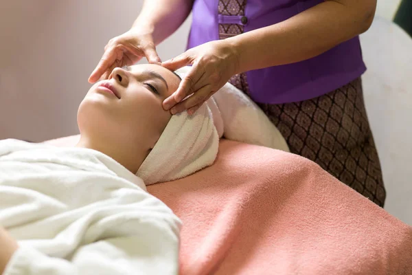 Mujer acostada con los ojos cerrados y masajeando cara o cabeza en el spa — Foto de Stock