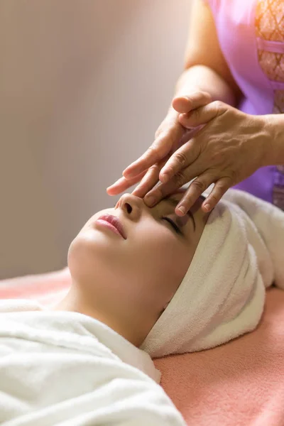 Mujer acostada con los ojos cerrados y masajeando cara o cabeza en el spa — Foto de Stock