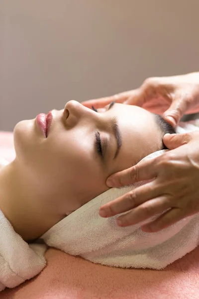 Mujer acostada con los ojos cerrados y masajeando cara o cabeza en el spa — Foto de Stock