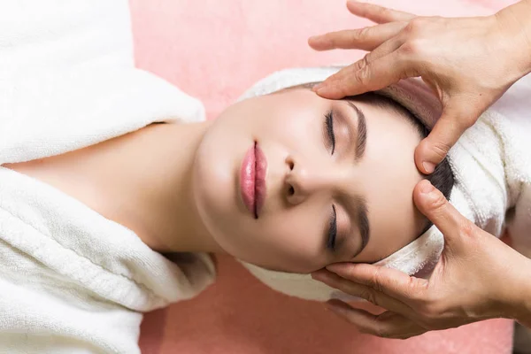 Mujer acostada con los ojos cerrados y masajeando cara o cabeza en el spa — Foto de Stock