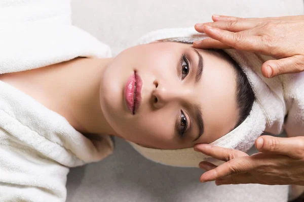 Mujer acostada con los ojos cerrados y masajeando cara o cabeza en el spa — Foto de Stock