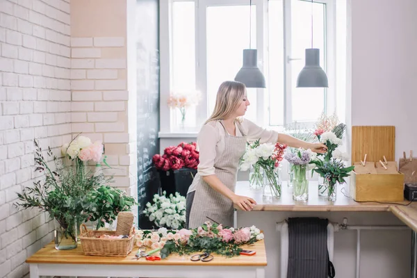 Sorrindo linda florista jovem arranjando plantas na loja de flores — Fotografia de Stock