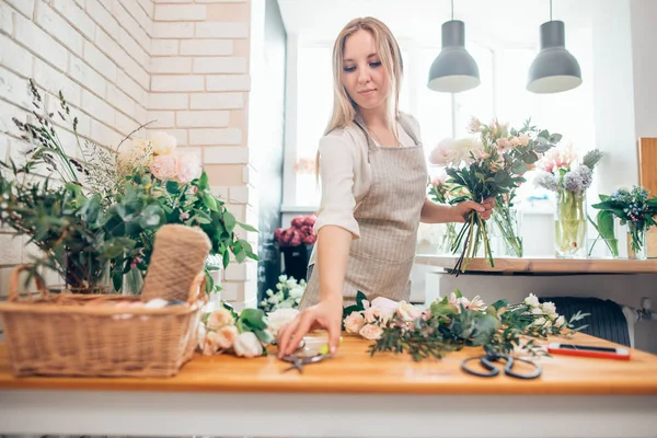 Smiling lovely young woman florist arranging plants in flower shop