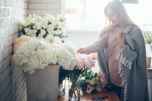 Smiling lovely young woman florist arranging plants in flower shop