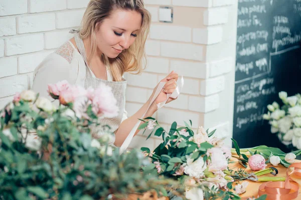 Händerna på florist mot skrivbordet med arbetsverktyg och band — Stockfoto