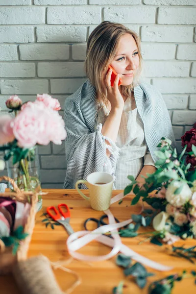 Jovem florista do sexo feminino falando no telefone e fazendo anotações na loja de flores . — Fotografia de Stock