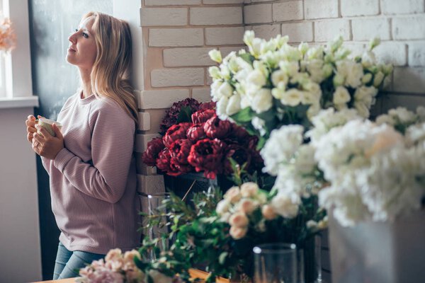 Florist woman in process of making bouquet, holds in her hand a cup of coffee