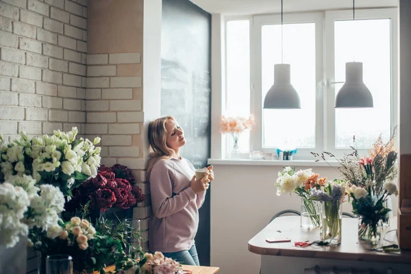 Buket, yapım sürecinde çiçekçi kadın tutan onun elinde bir fincan kahve