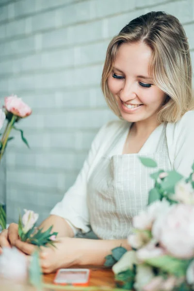 Sonriente encantadora florista joven que arregla las plantas en la tienda de flores — Foto de Stock