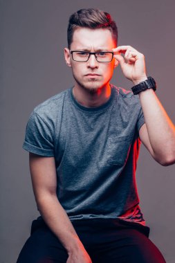 Gözlüklü adam, Gri Duvara Karşı Kamera 'ya bakıyor.