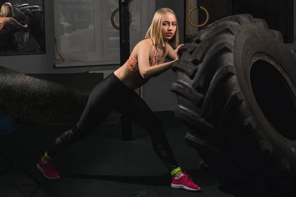Ajuste atleta femenina haciendo ejercicio con un neumático enorme, girando y volteando en el gimnasio — Foto de Stock
