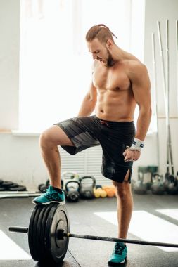 genç adam halter eğitim salonunda için hazırlanıyor. bacağını halter koymak