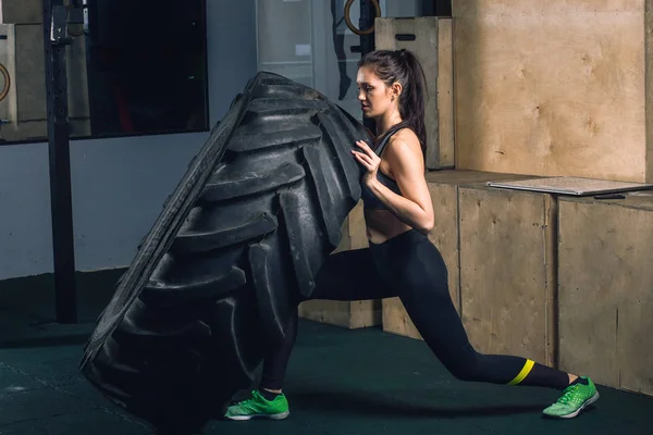 Chica fuerte volteando un neumático en el gimnasio . — Foto de Stock